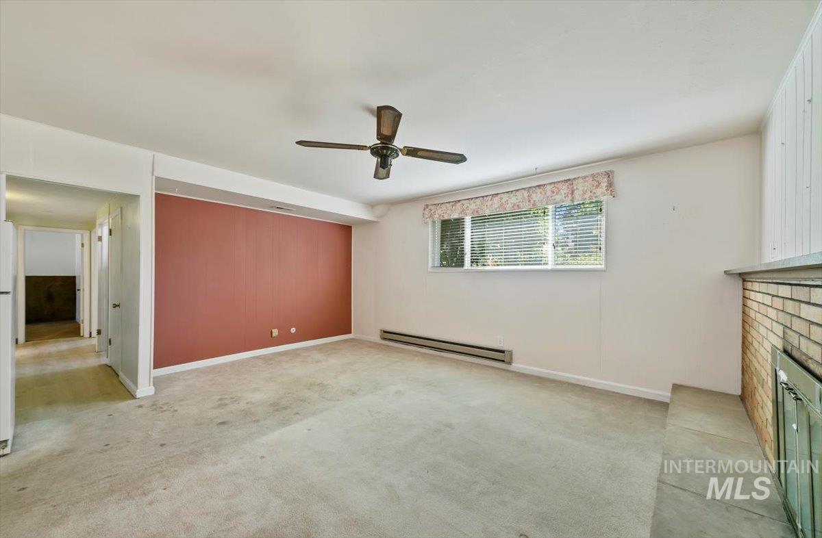 Unfurnished living room with a baseboard heating unit, light carpet, a brick fireplace, and a ceiling fan