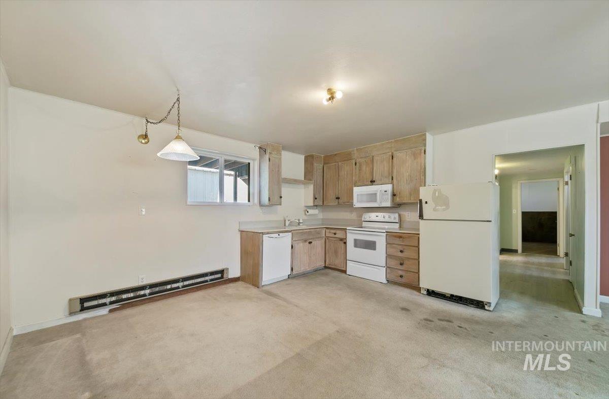 Kitchen featuring white appliances, a baseboard heating unit, light colored carpet, light countertops, and hanging light fixtures