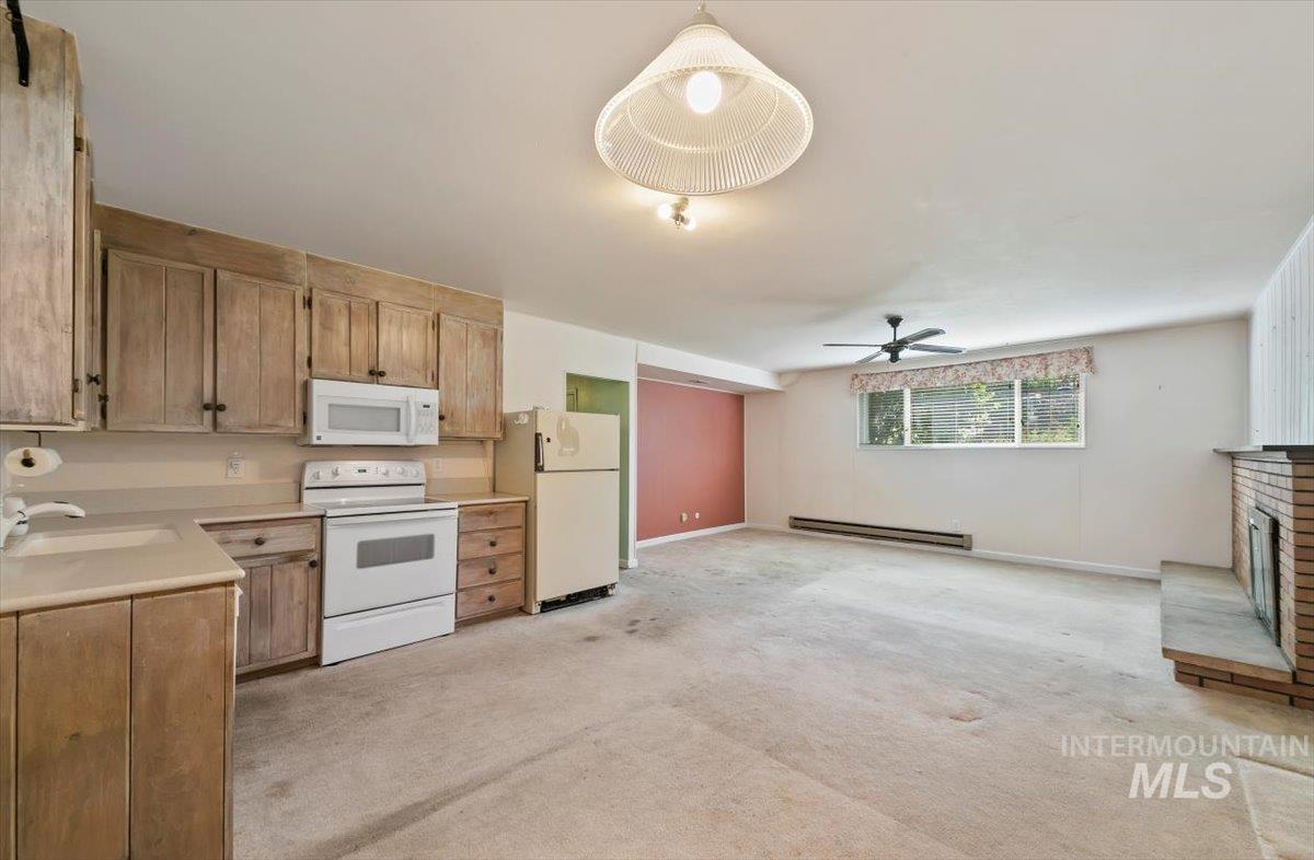 Kitchen featuring white appliances, light countertops, light carpet, a baseboard radiator, and a ceiling fan