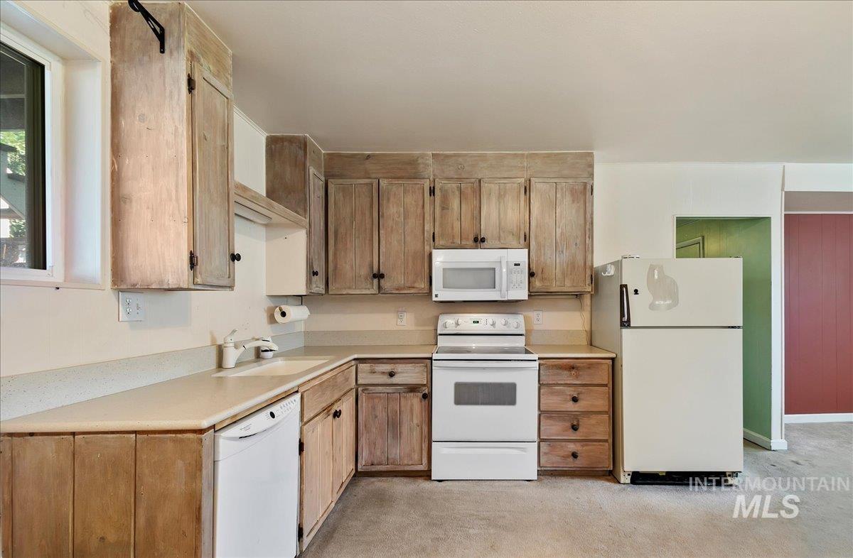Kitchen with white appliances, light countertops, and light carpet