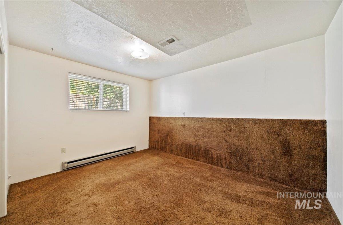 Empty room with baseboard heating, carpet floors, and a textured ceiling