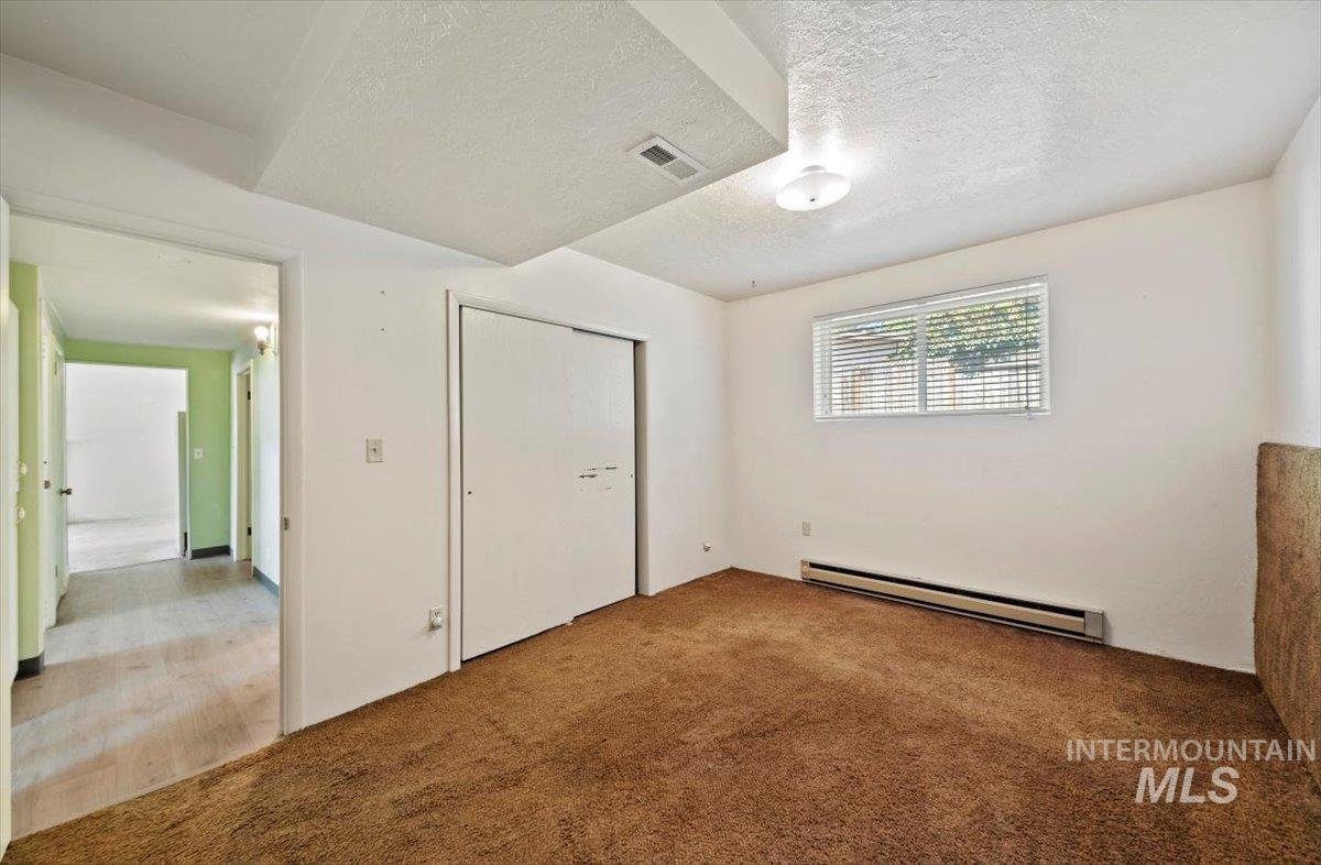 Unfurnished bedroom featuring baseboard heating, a textured ceiling, carpet, and a closet