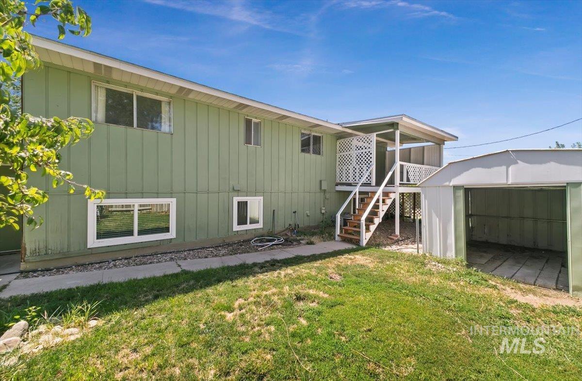 Back of property with stairs, board and batten siding, a yard, a storage unit, and a garage