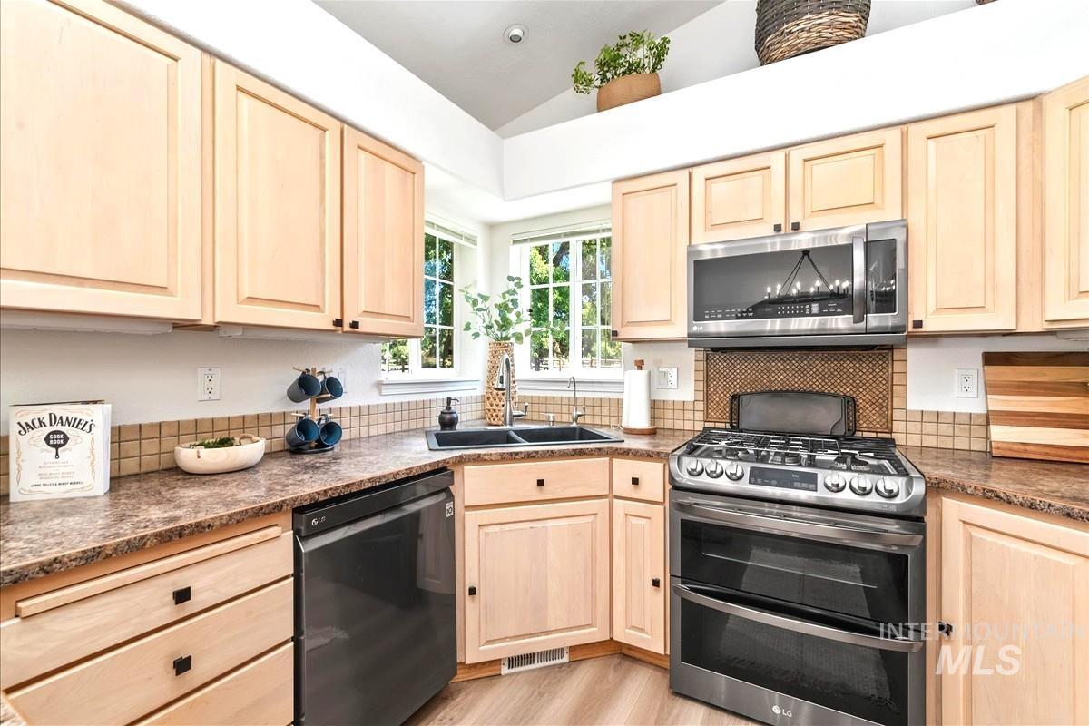 Kitchen featuring light brown cabinets, stainless steel appliances, light wood-type flooring, and lofted ceiling