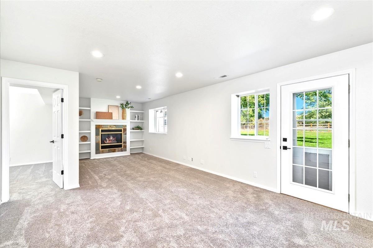 Unfurnished living room with light carpet, recessed lighting, a tile fireplace, and built in shelves