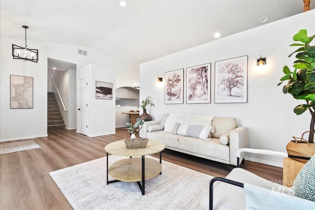 Living room featuring vaulted ceiling, wood finished floors, stairs, recessed lighting, and a chandelier