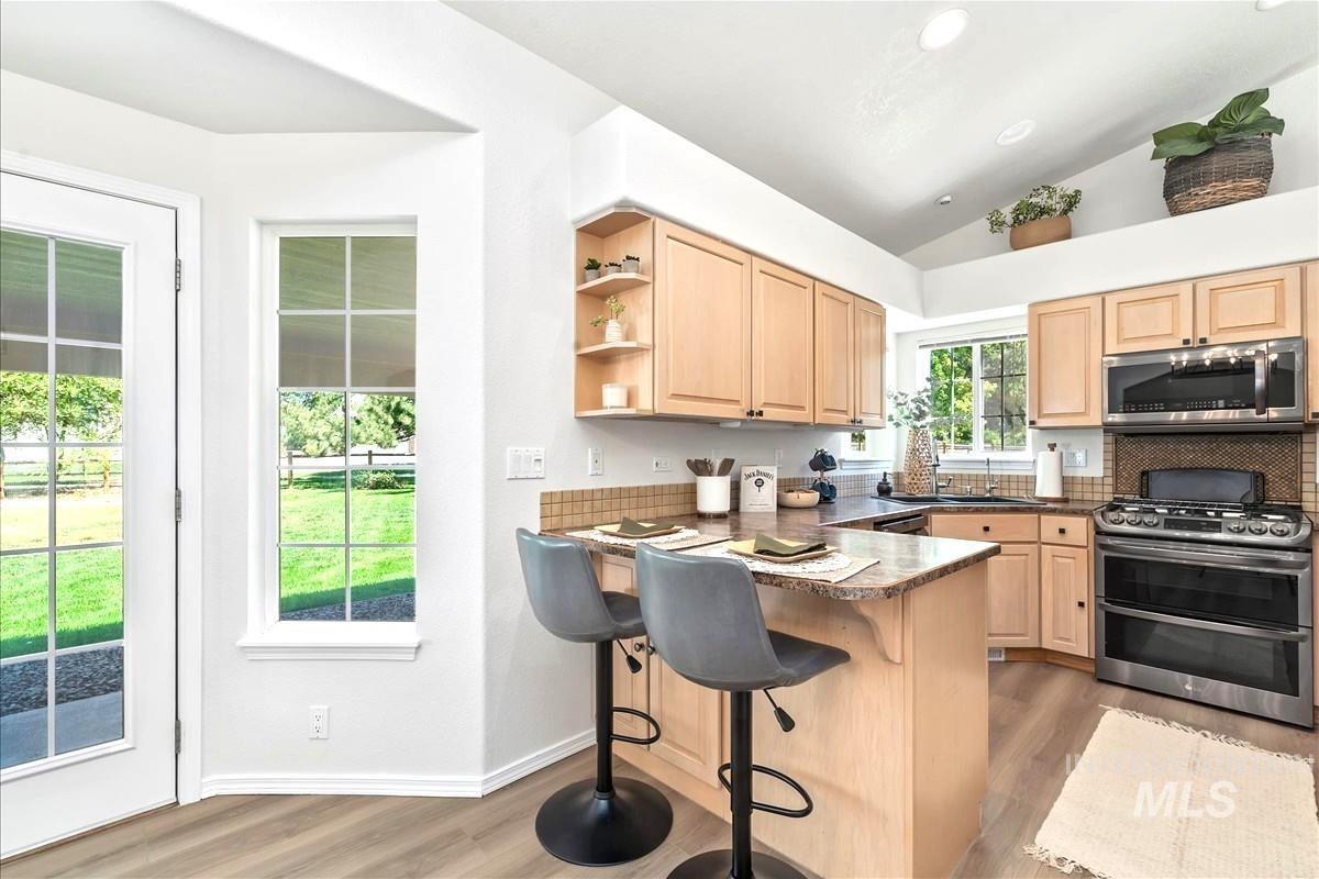 Kitchen featuring light brown cabinets, open shelves, stainless steel appliances, lofted ceiling, and recessed lighting