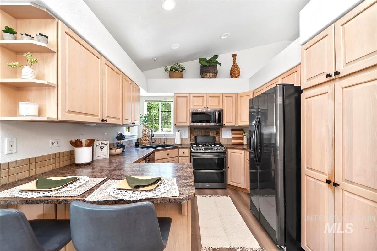 Kitchen with light brown cabinetry, lofted ceiling, appliances with stainless steel finishes, a kitchen breakfast bar, and recessed lighting