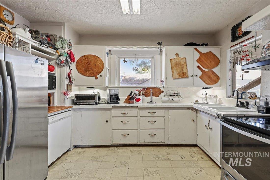 Kitchen featuring appliances with stainless steel finishes, light countertops, light flooring, white cabinetry, and a textured ceiling
