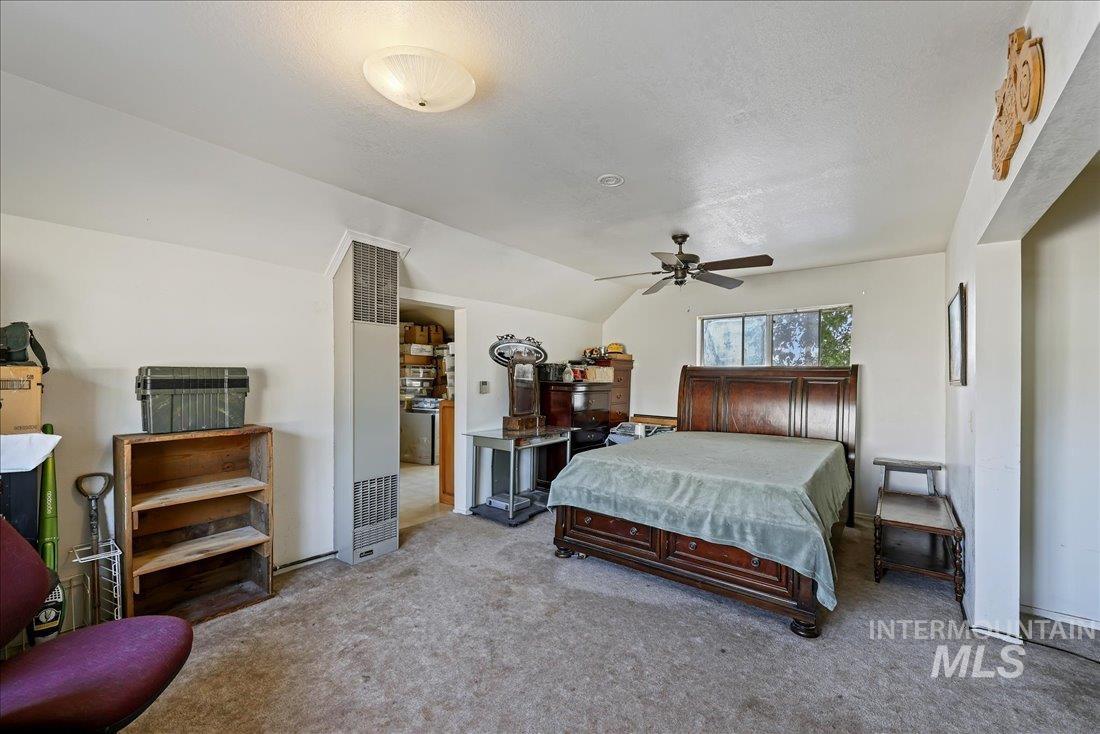 Carpeted bedroom featuring lofted ceiling, a heating unit, ceiling fan, and a textured ceiling