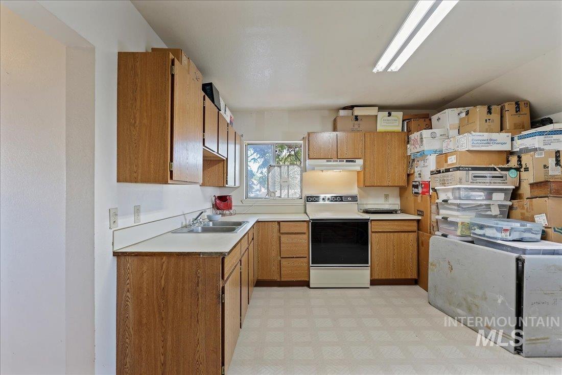 Kitchen featuring white electric stove, light countertops, brown cabinets, light flooring, and under cabinet range hood