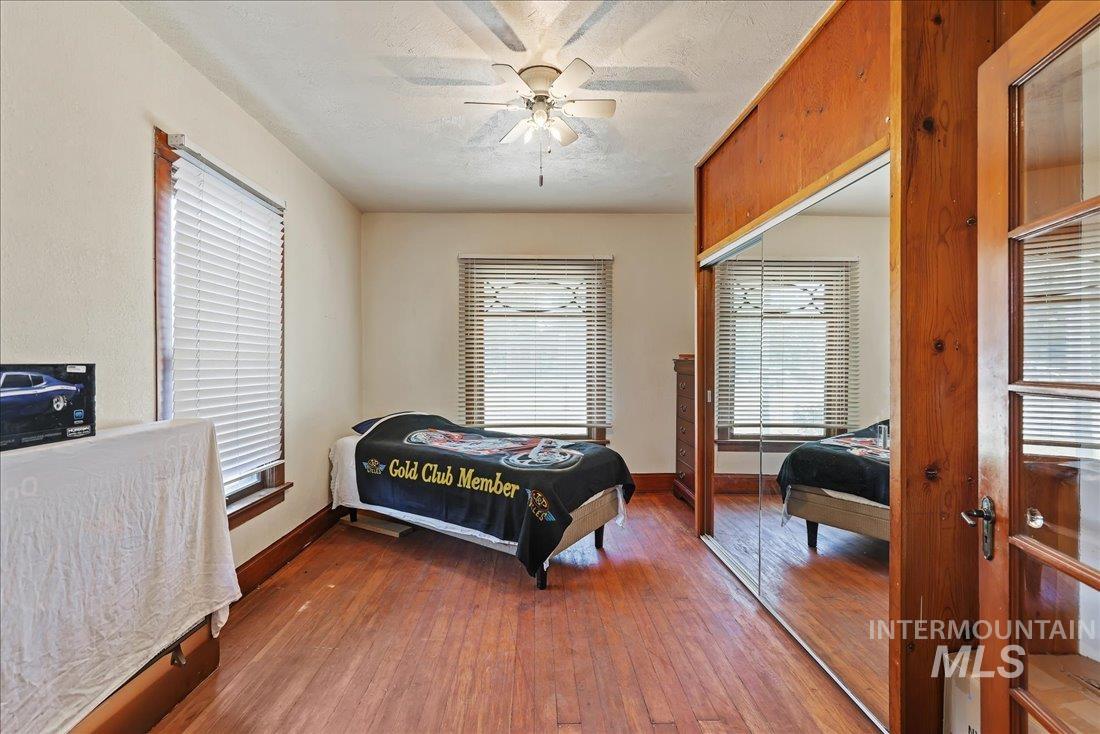 Bedroom with dark wood-style floors, a ceiling fan, a closet, multiple windows, and a textured ceiling