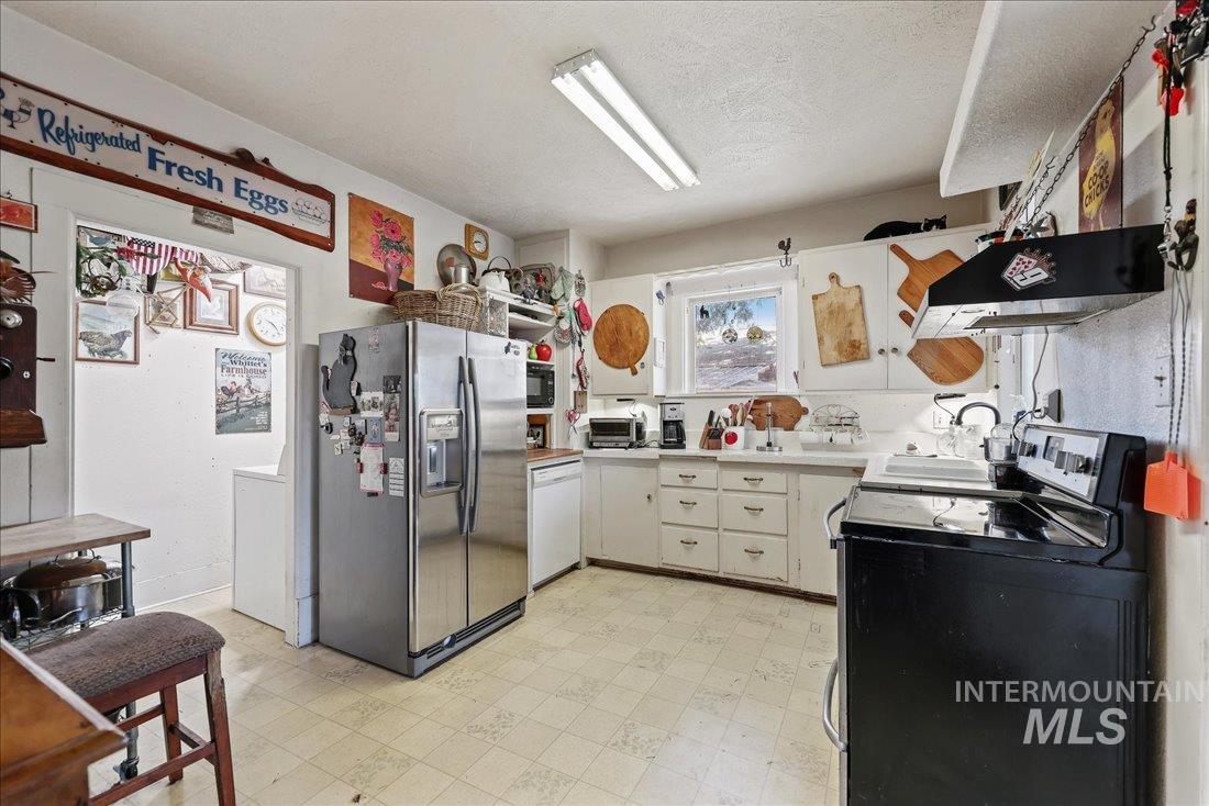 Kitchen featuring stainless steel refrigerator with ice dispenser, light flooring, electric stove, light countertops, and white cabinets