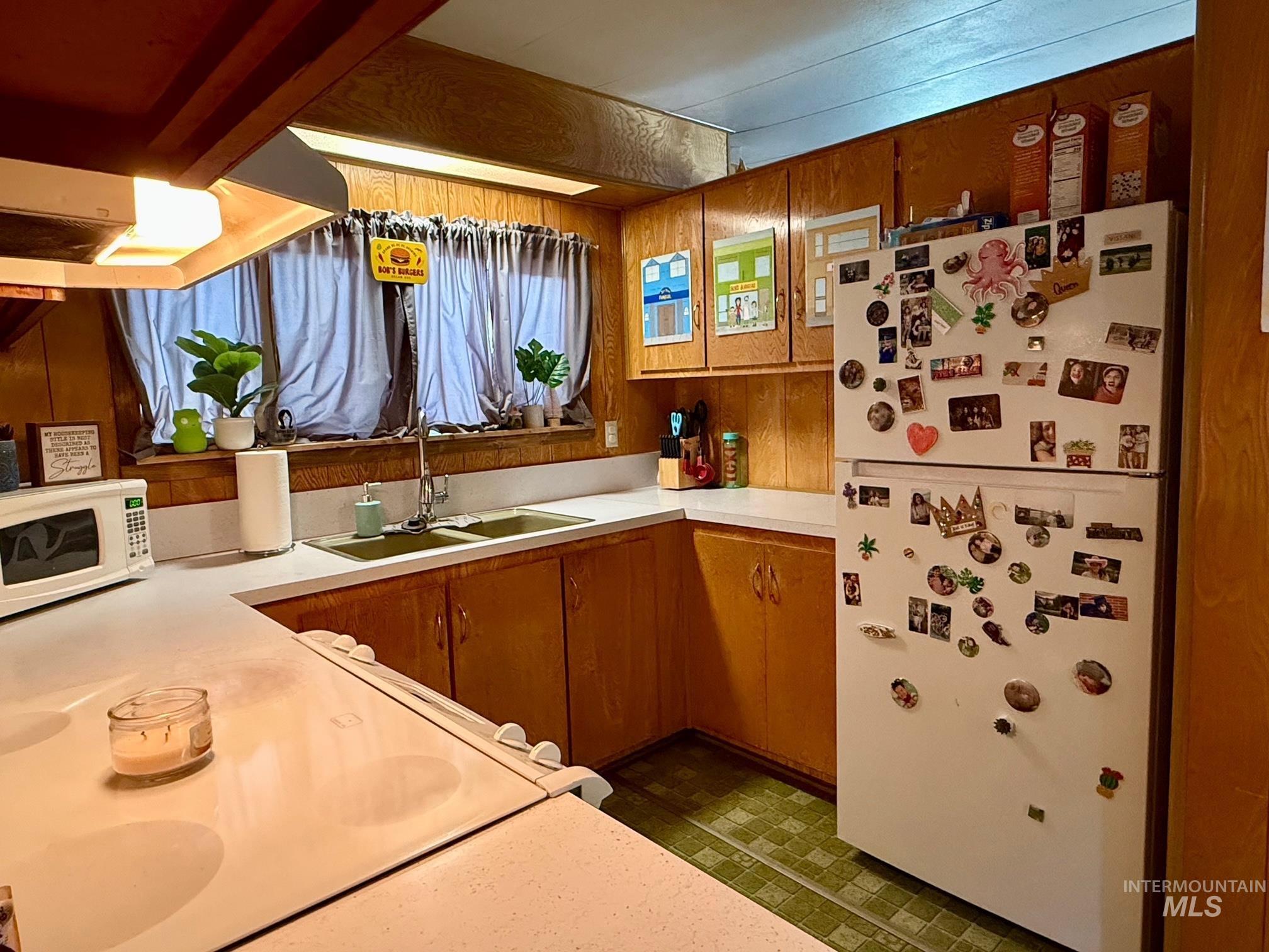 Kitchen with light countertops, white appliances, wood walls, and brown cabinets