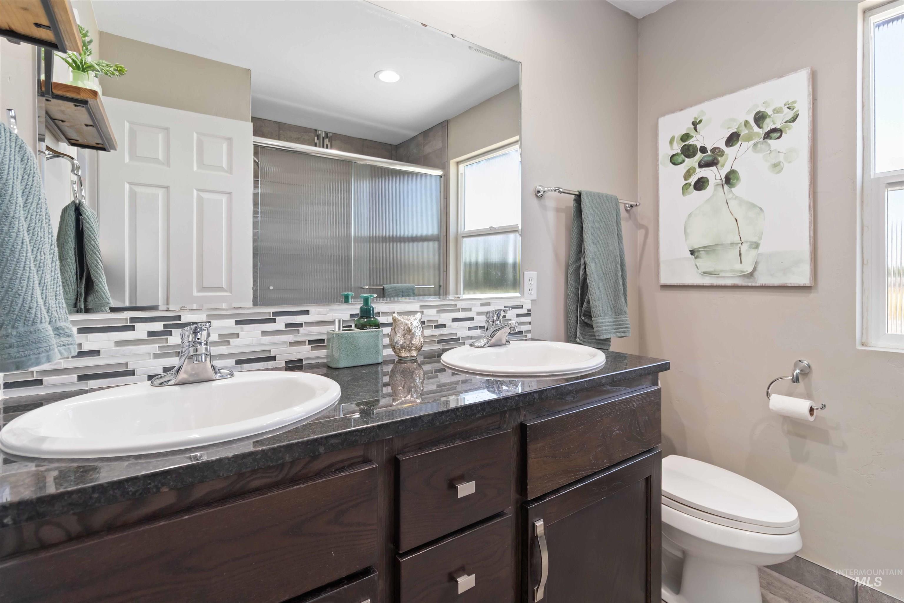 Full bathroom with backsplash, double vanity, and a shower stall