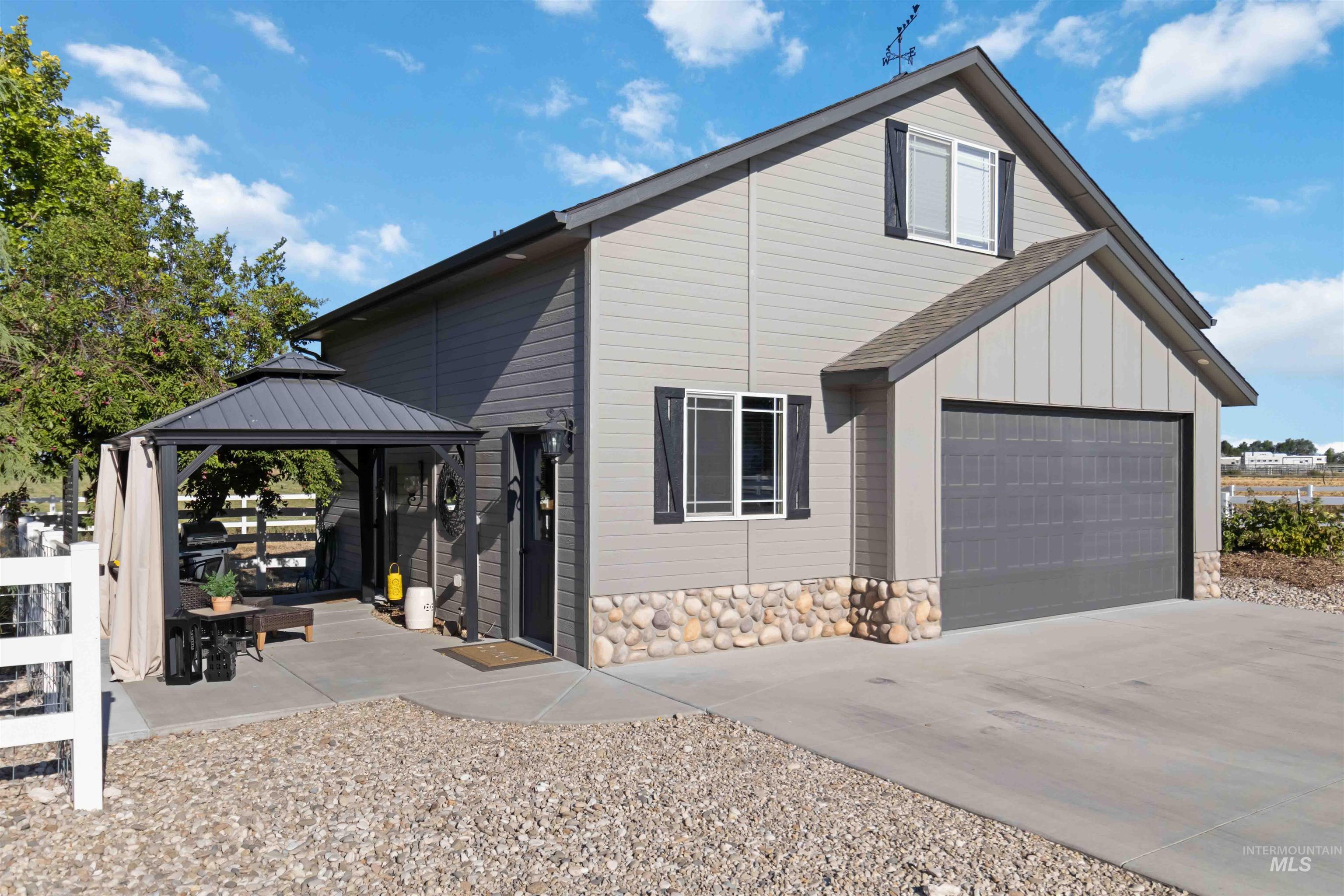 View of home's exterior featuring driveway, a patio, a garage, a gazebo, and stone siding