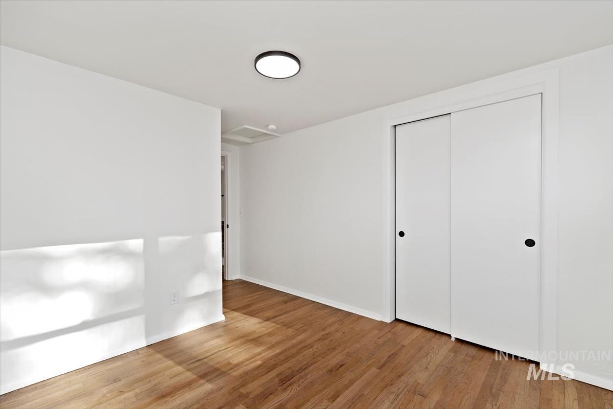 Unfurnished bedroom featuring light wood finished floors, a closet, and attic access