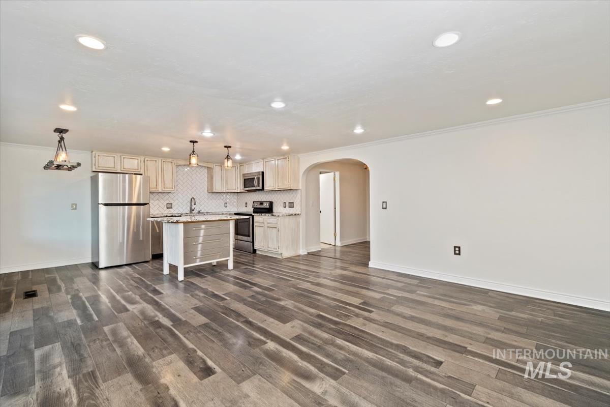Kitchen featuring arched walkways, appliances with stainless steel finishes, a kitchen island, ornamental molding, and open floor plan