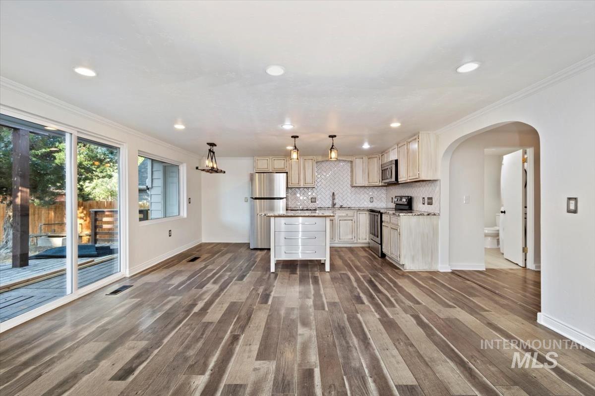 Kitchen with arched walkways, ornamental molding, stainless steel appliances, a kitchen island, and hanging light fixtures