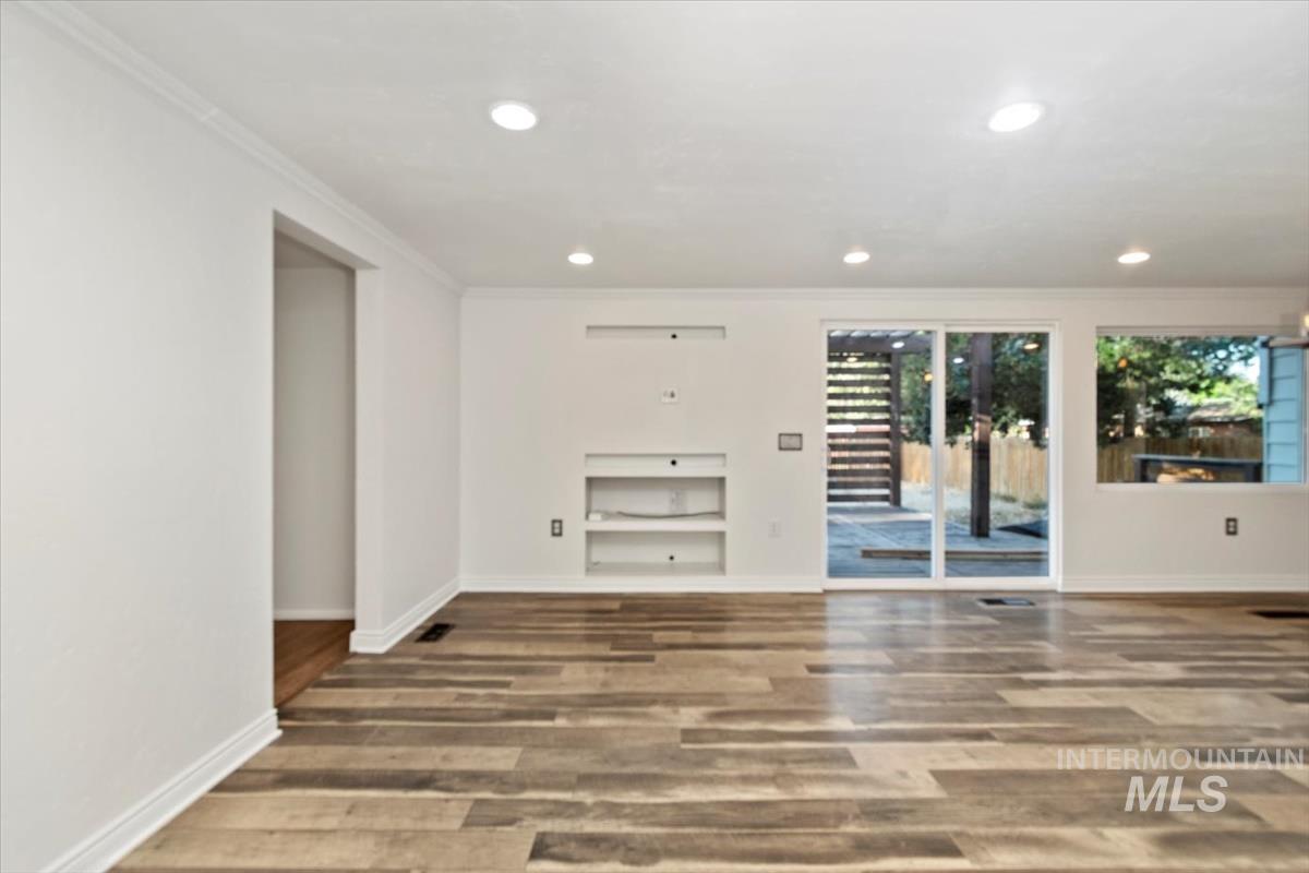 Unfurnished living room with ornamental molding, wood finished floors, recessed lighting, and built in shelves