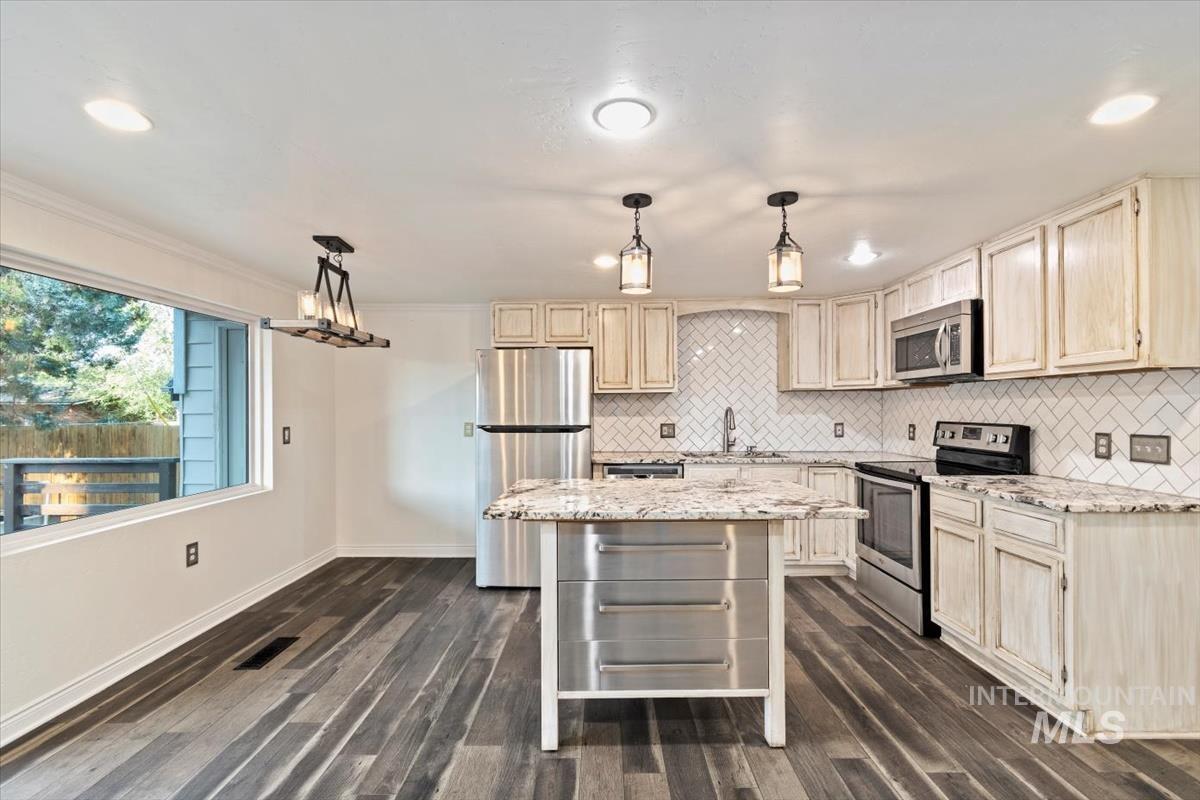 Kitchen with appliances with stainless steel finishes, hanging light fixtures, light stone counters, recessed lighting, and crown molding
