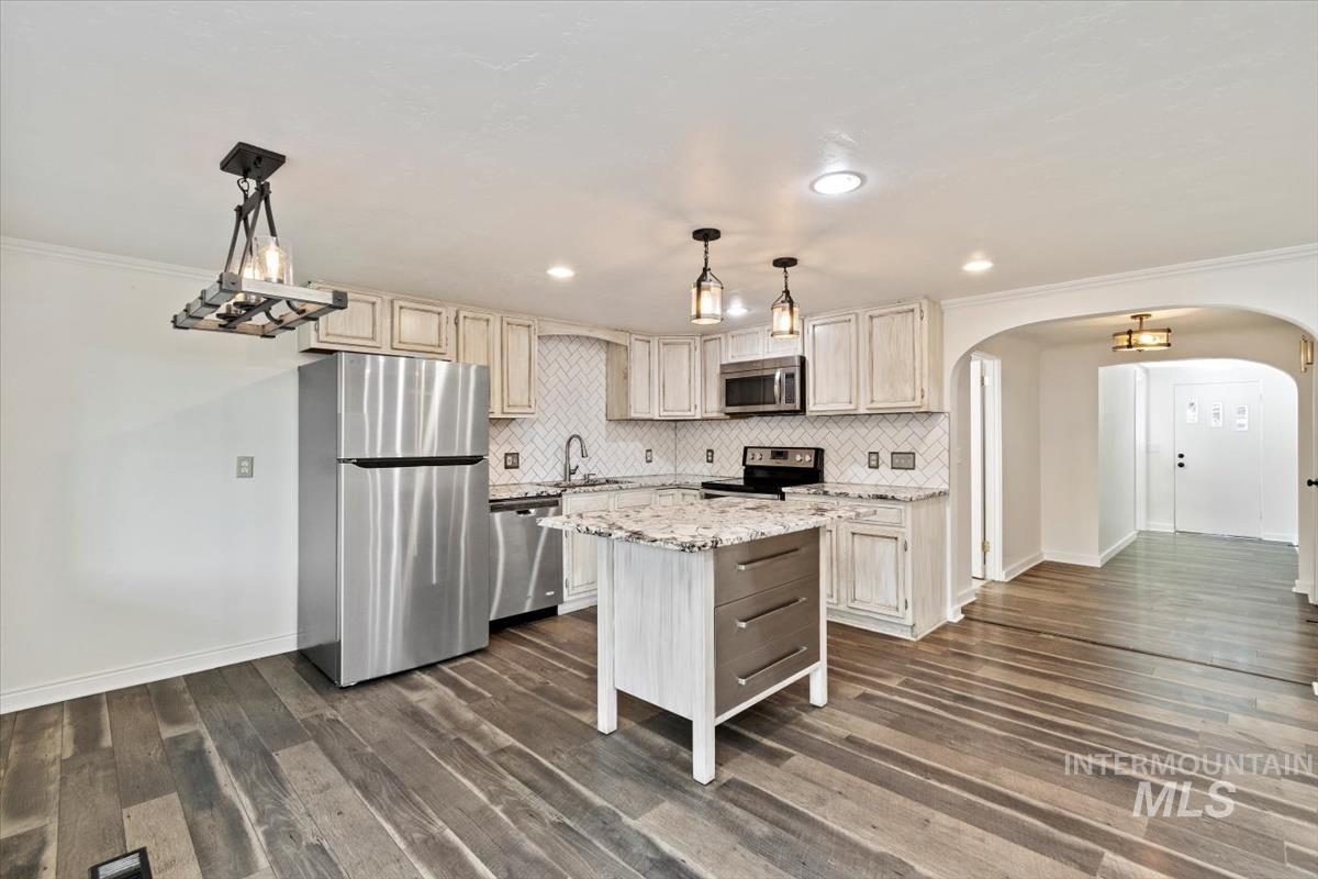 Kitchen featuring appliances with stainless steel finishes, ornamental molding, hanging light fixtures, light stone countertops, and arched walkways