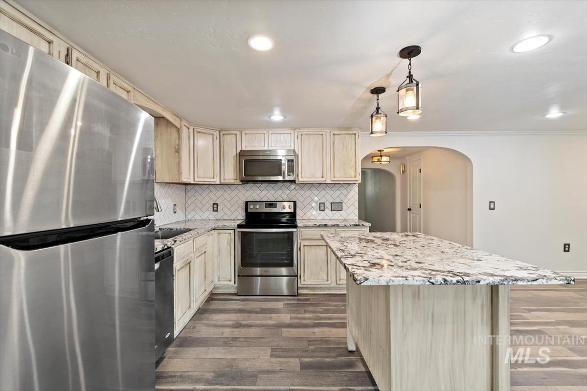 Kitchen featuring stainless steel appliances, tasteful backsplash, hanging light fixtures, dark wood finished floors, and light stone countertops