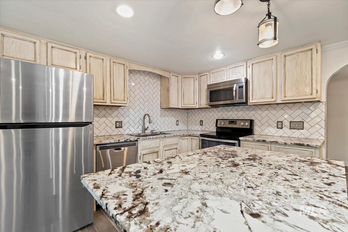 Kitchen featuring appliances with stainless steel finishes, light stone countertops, decorative backsplash, arched walkways, and light brown cabinets