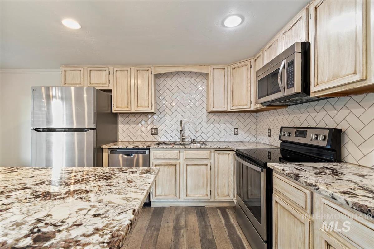 Kitchen featuring appliances with stainless steel finishes, tasteful backsplash, light brown cabinets, light stone counters, and recessed lighting