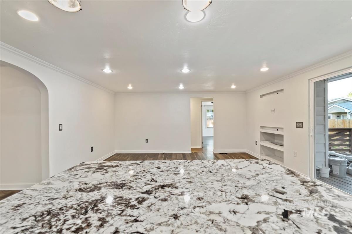 Empty room with wood finished floors, plenty of natural light, arched walkways, recessed lighting, and crown molding