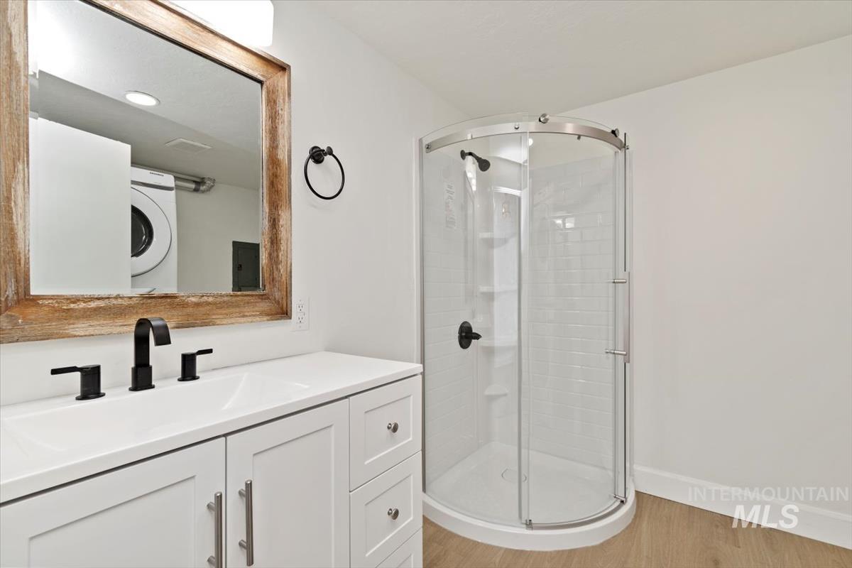 Bathroom with a stall shower, vanity, light wood-style floors, and stacked washer / dryer