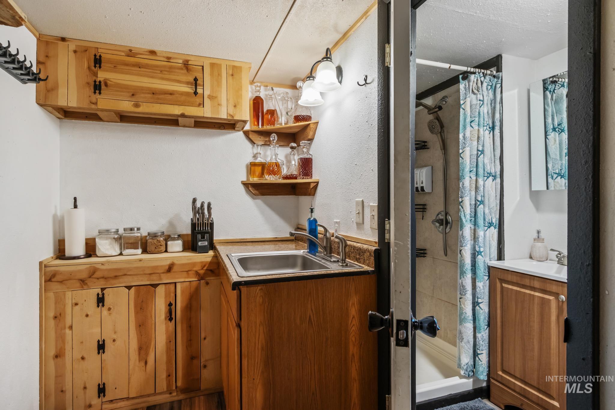 Indoor wet bar with brown cabinetry, a textured ceiling, open shelves, and light countertops