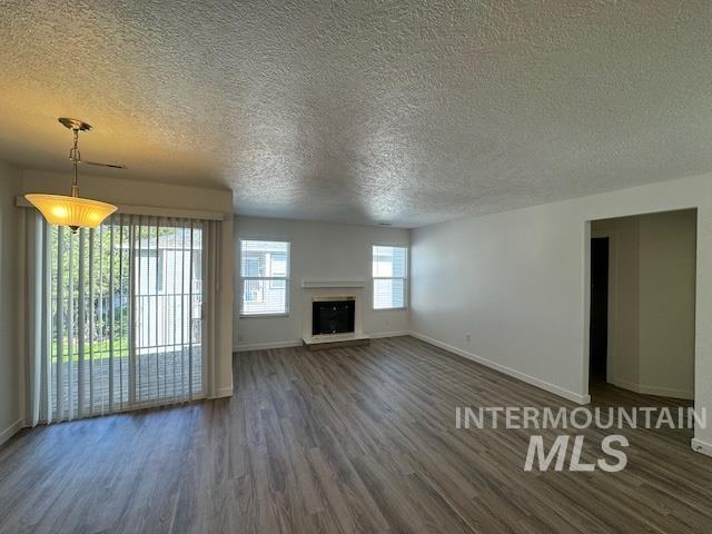 Unfurnished living room with a textured ceiling, dark wood-type flooring, and a fireplace with raised hearth