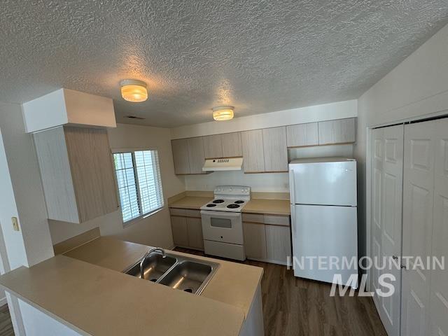 Kitchen with white appliances, dark wood finished floors, light countertops, a textured ceiling, and a peninsula