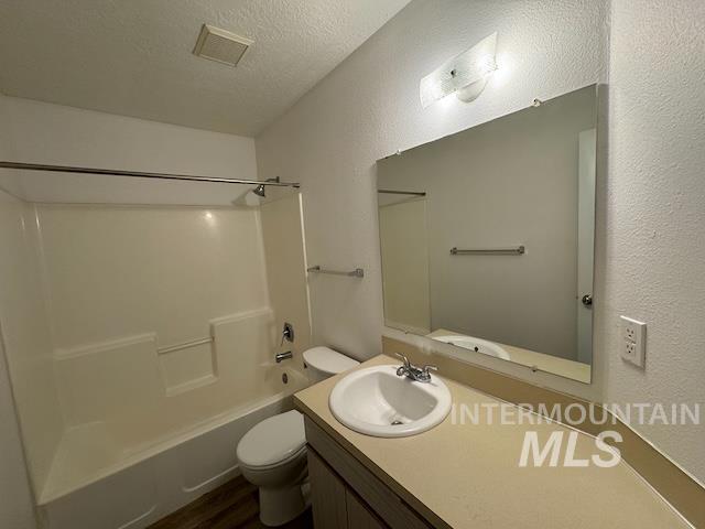 Full bathroom featuring a textured ceiling, shower / washtub combination, a textured wall, vanity, and dark wood-style flooring