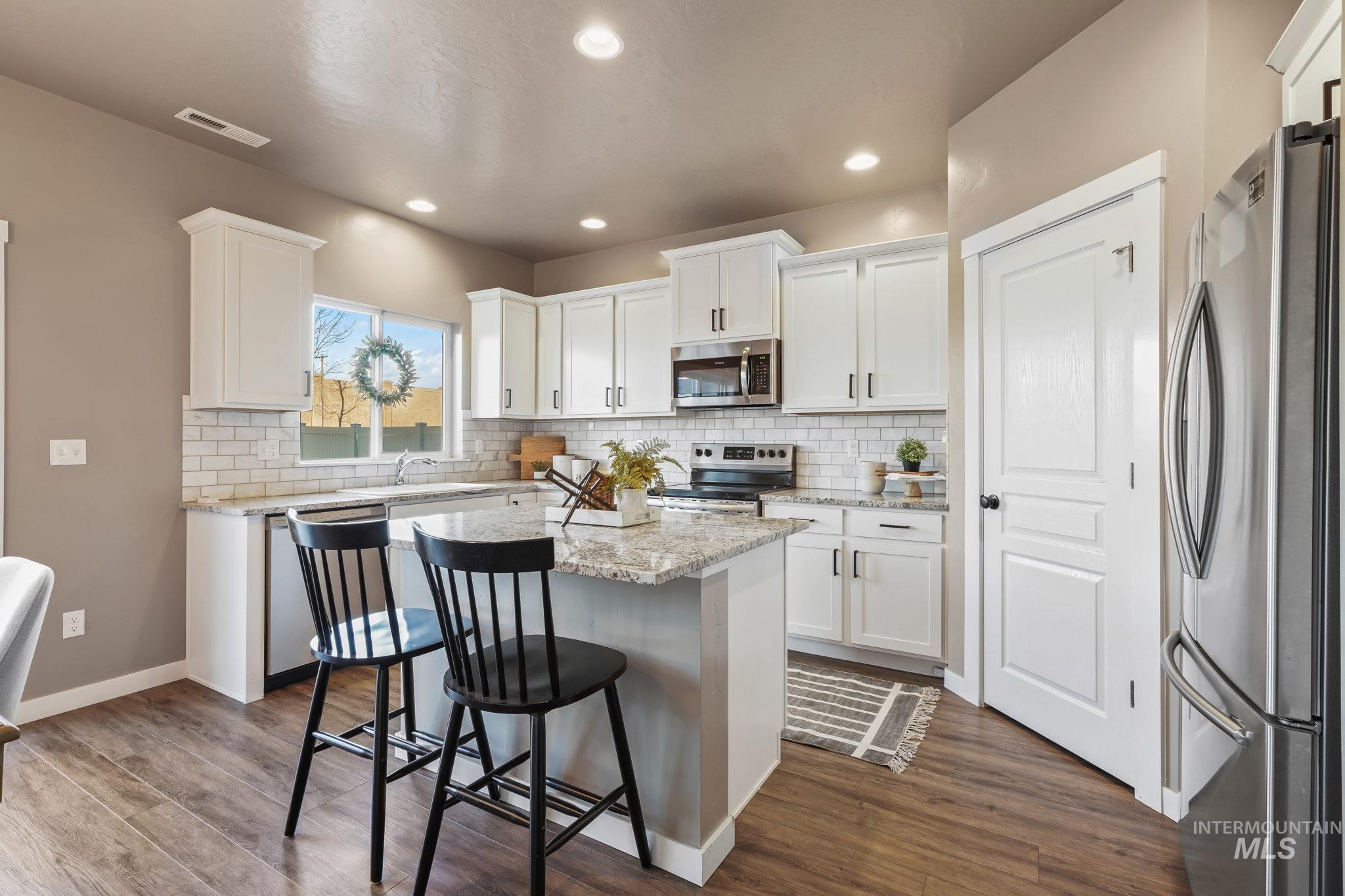 Kitchen featuring light stone counters, white cabinetry, stainless steel appliances, a kitchen bar, and recessed lighting
