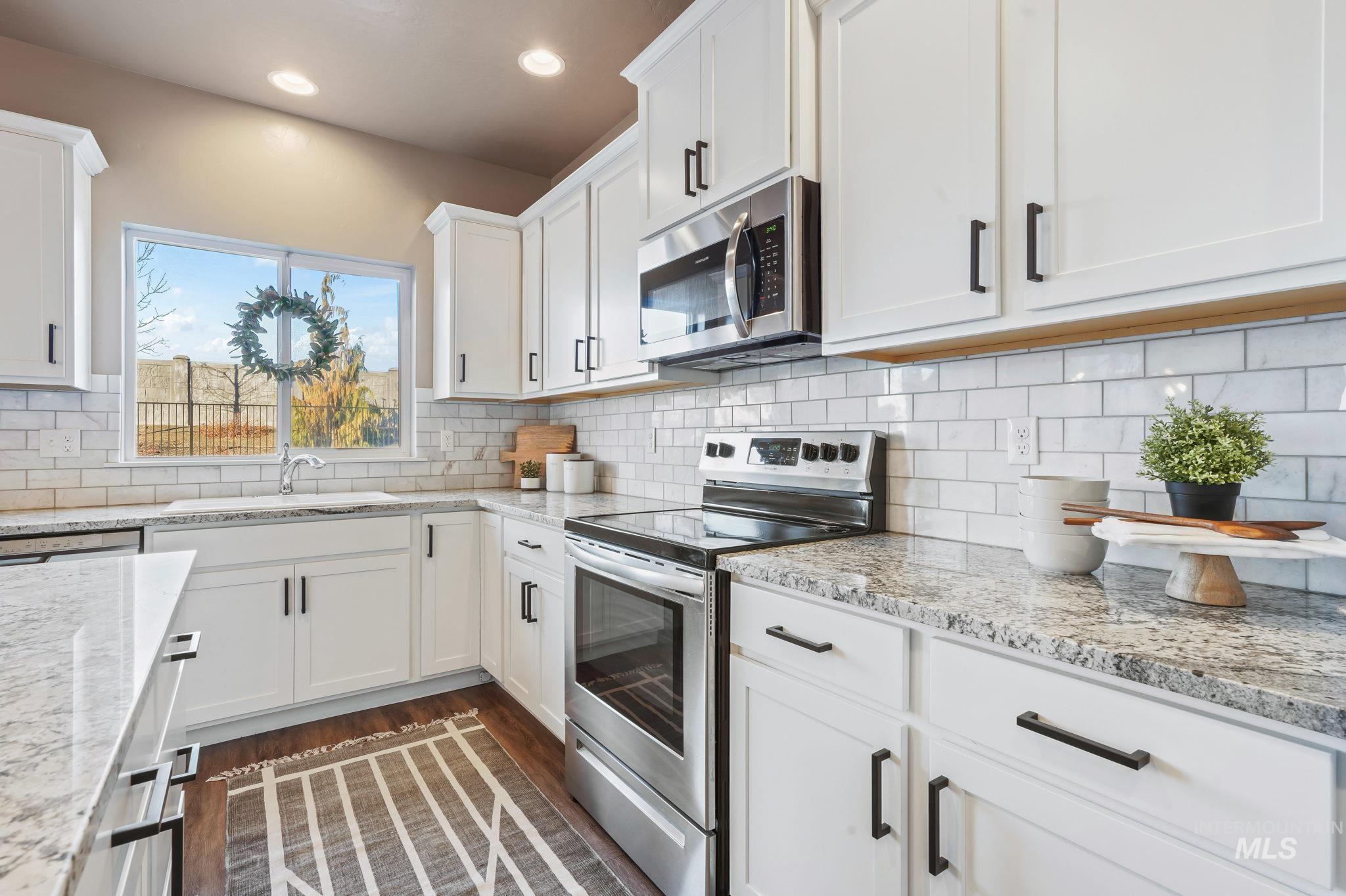Kitchen featuring stainless steel appliances, white cabinets, dark wood finished floors, light stone counters, and recessed lighting