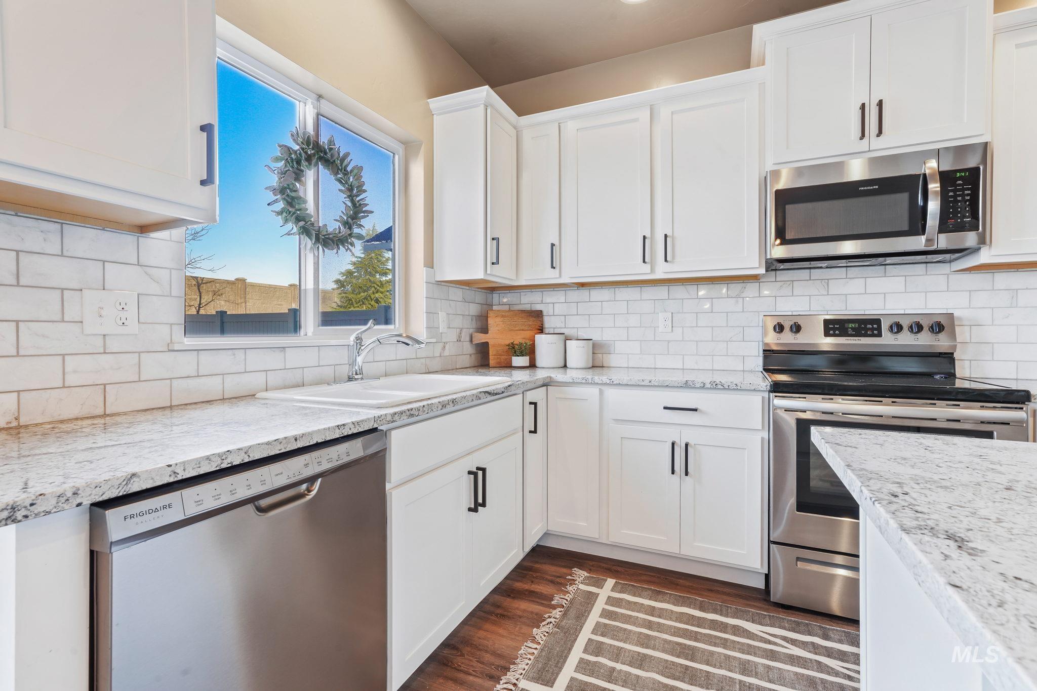 Kitchen featuring stainless steel appliances, dark wood-type flooring, white cabinets, and tasteful backsplash