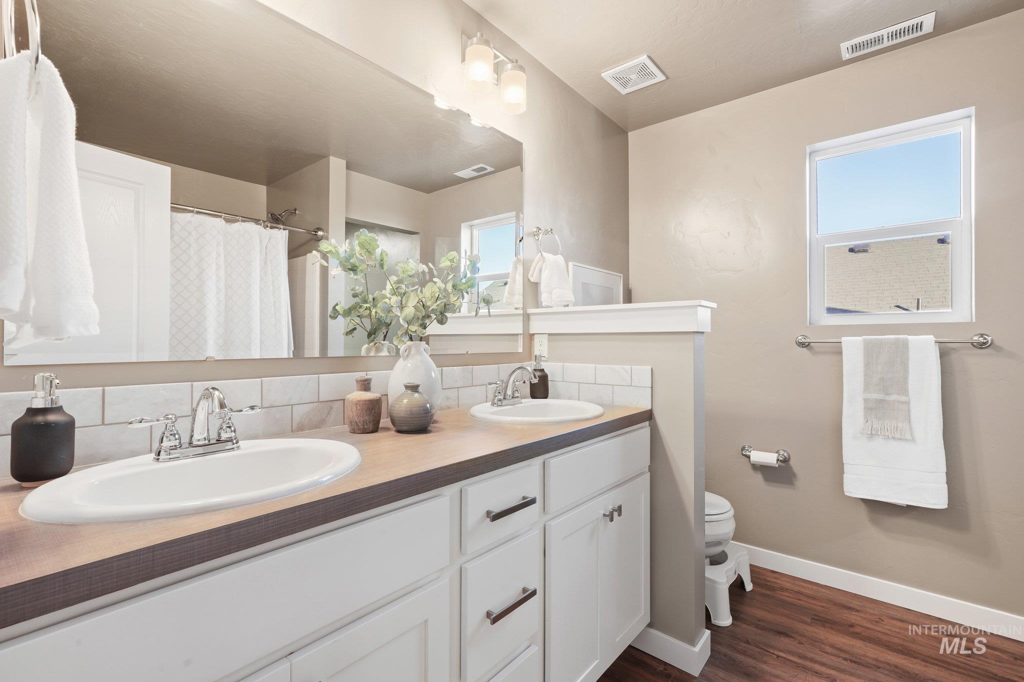 Bathroom with dark wood-style floors, double vanity, backsplash, and curtained shower