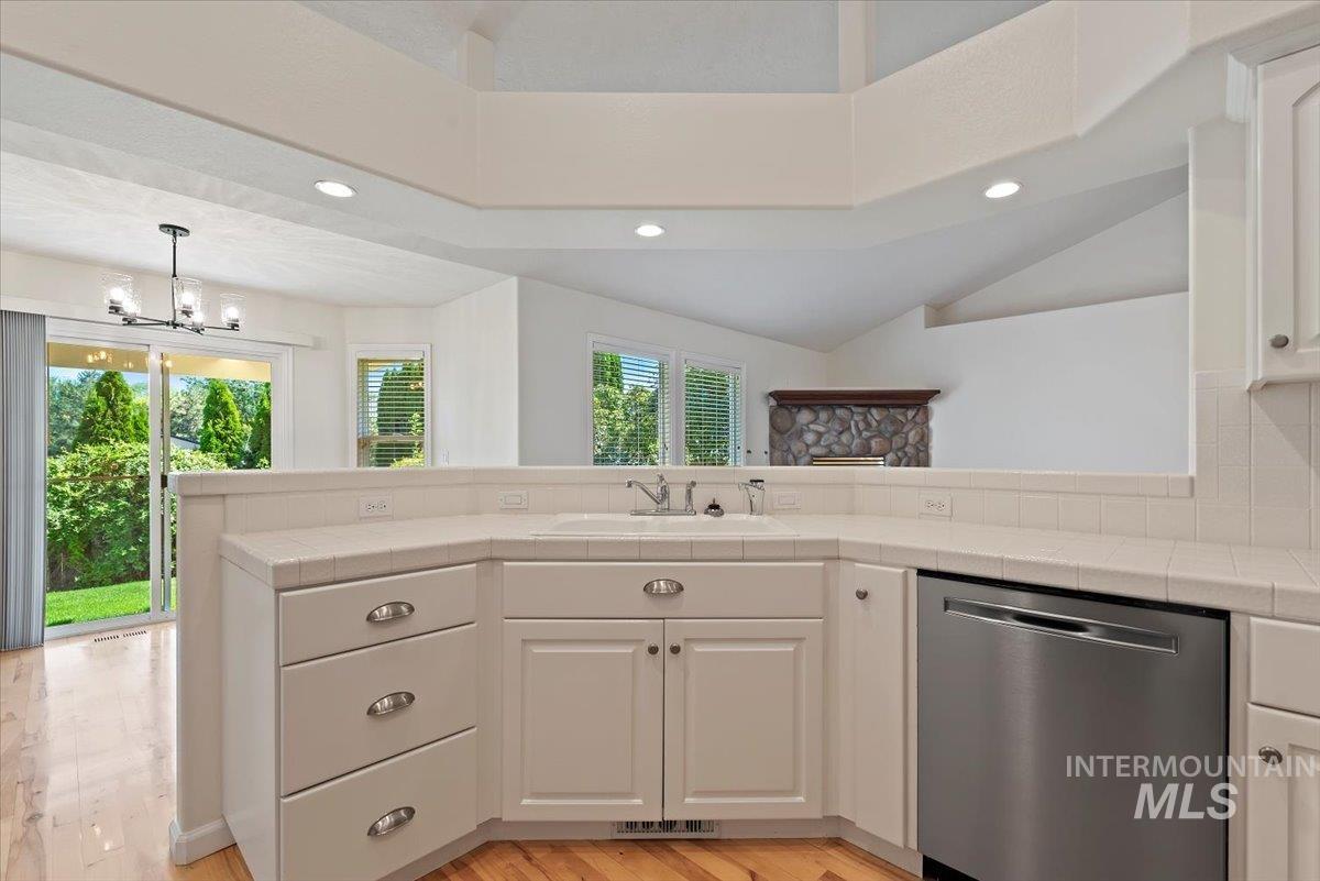Kitchen with tile counters, recessed lighting, stainless steel dishwasher, white cabinetry, and decorative light fixtures