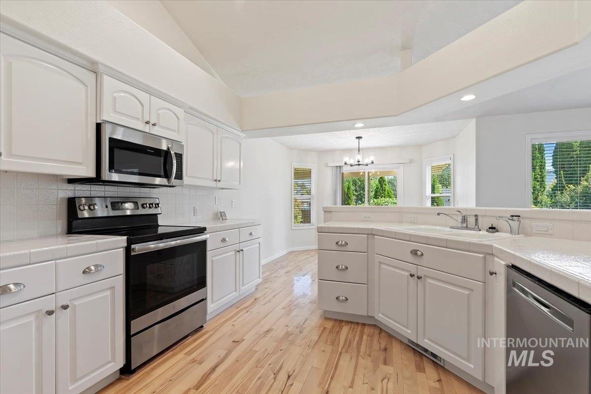 Kitchen featuring stainless steel appliances, tile counters, recessed lighting, light wood-type flooring, and a chandelier