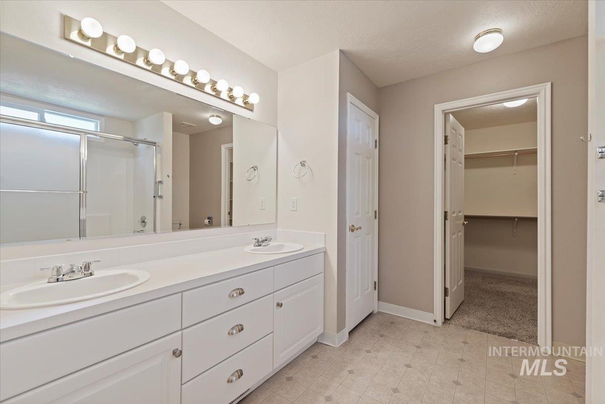 Bathroom featuring a shower stall, double vanity, a walk in closet, and a textured ceiling