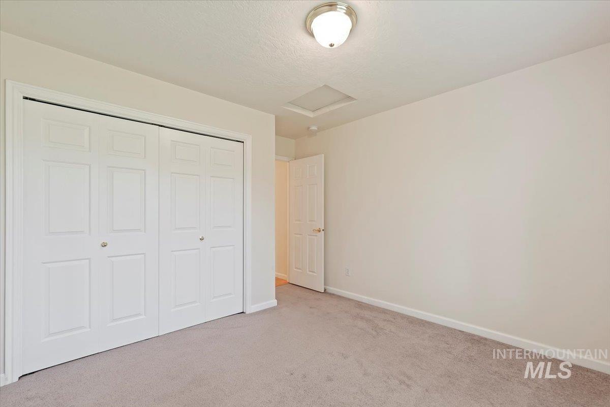 Unfurnished bedroom with attic access, carpet floors, a closet, and a textured ceiling