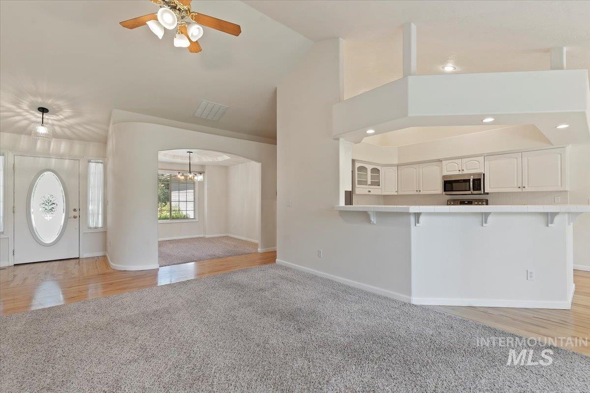 Unfurnished living room with light wood-type flooring, a ceiling fan, light carpet, high vaulted ceiling, and a chandelier