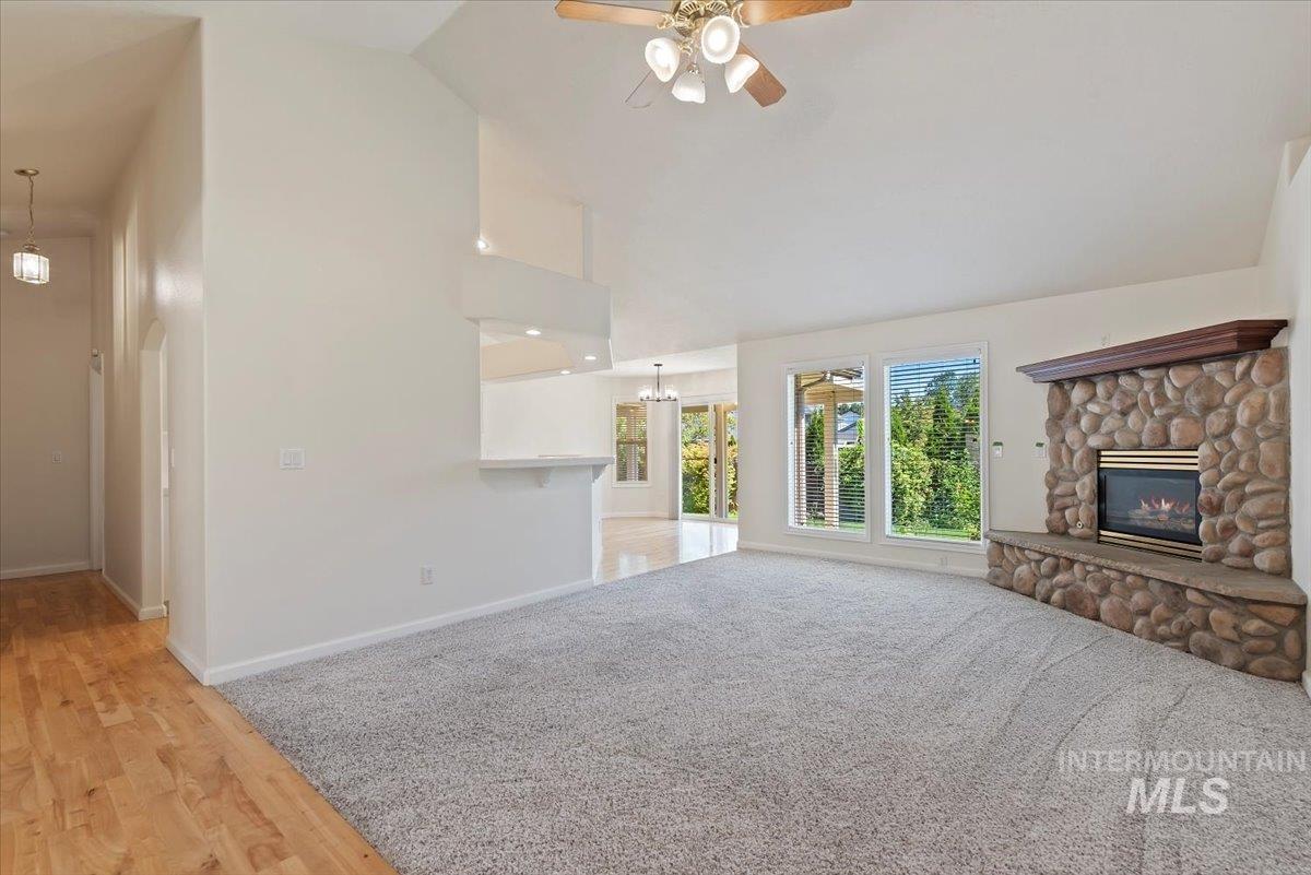Unfurnished living room featuring a ceiling fan, light wood-style floors, high vaulted ceiling, a stone fireplace, and a chandelier