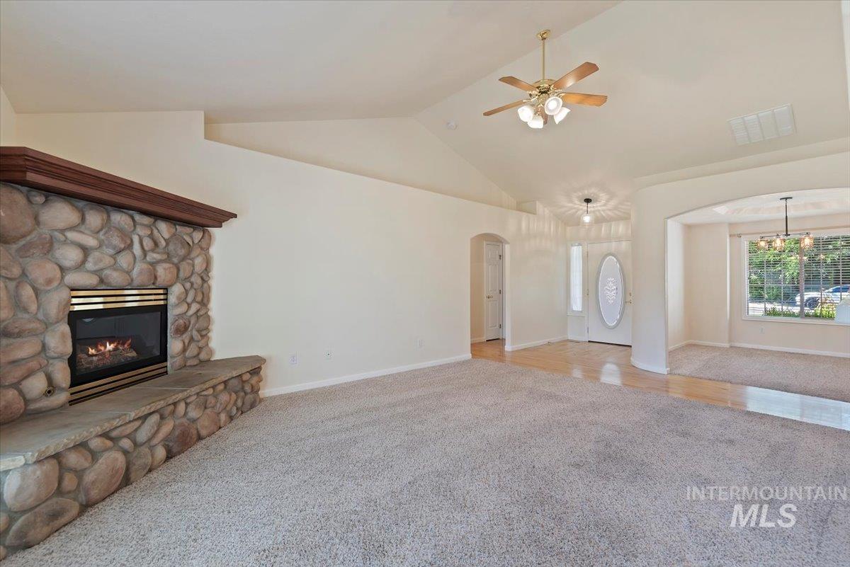 Unfurnished living room featuring carpet, a stone fireplace, arched walkways, high vaulted ceiling, and ceiling fan