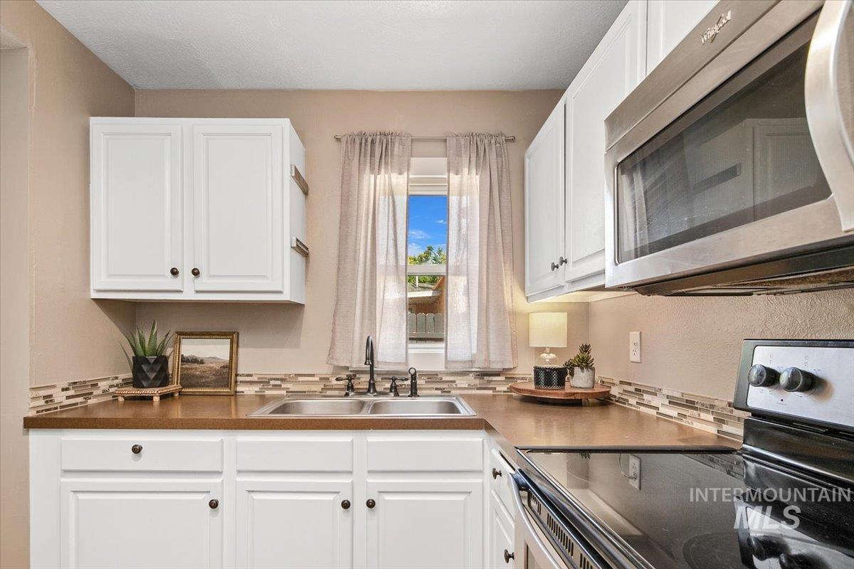 Kitchen with stainless steel appliances, white cabinetry, and tasteful backsplash