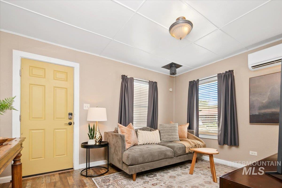 Living room with wood finished floors, a wall mounted AC, and crown molding