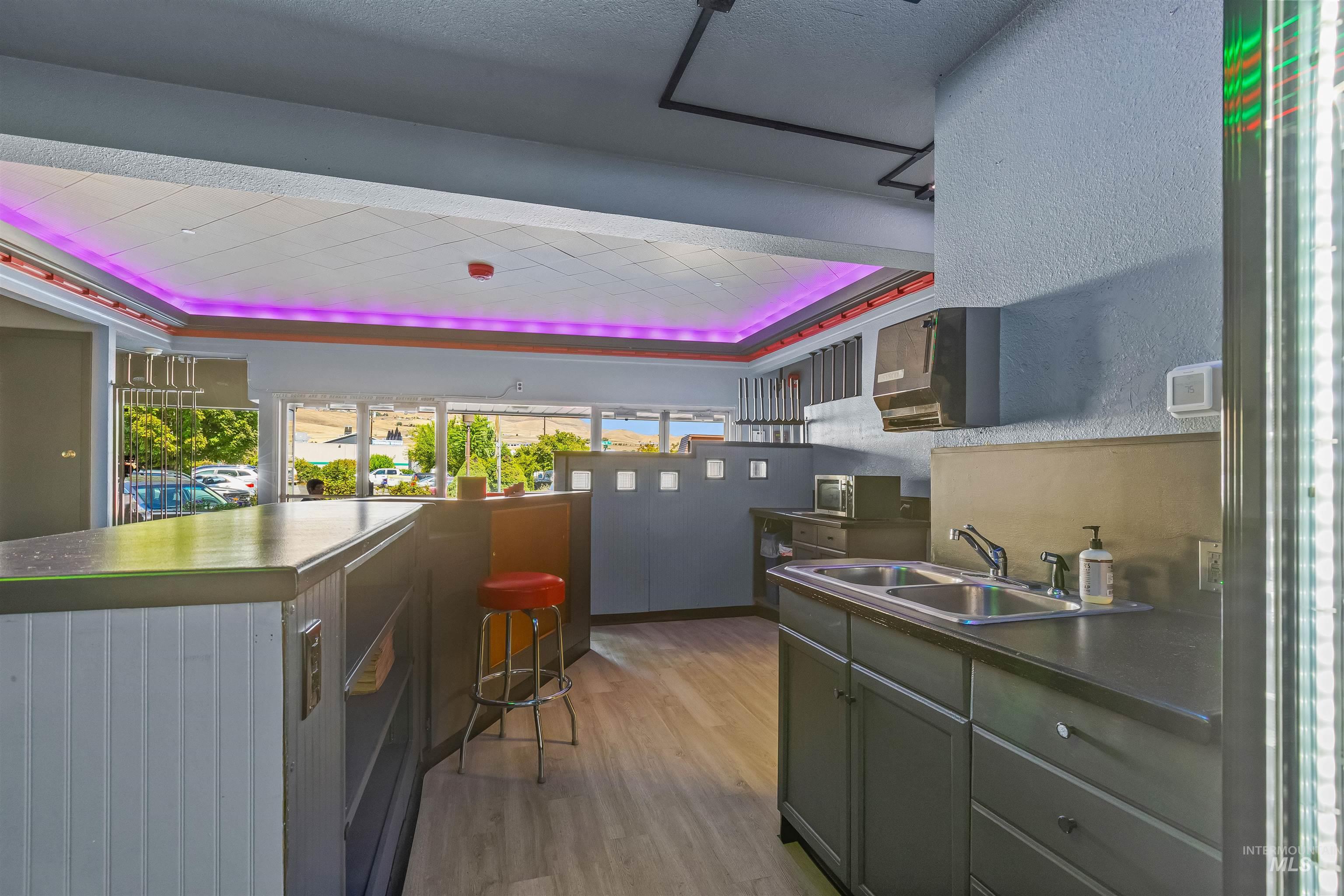 Kitchen with a raised ceiling, light wood-type flooring, dark countertops, a breakfast bar area, and stainless steel microwave