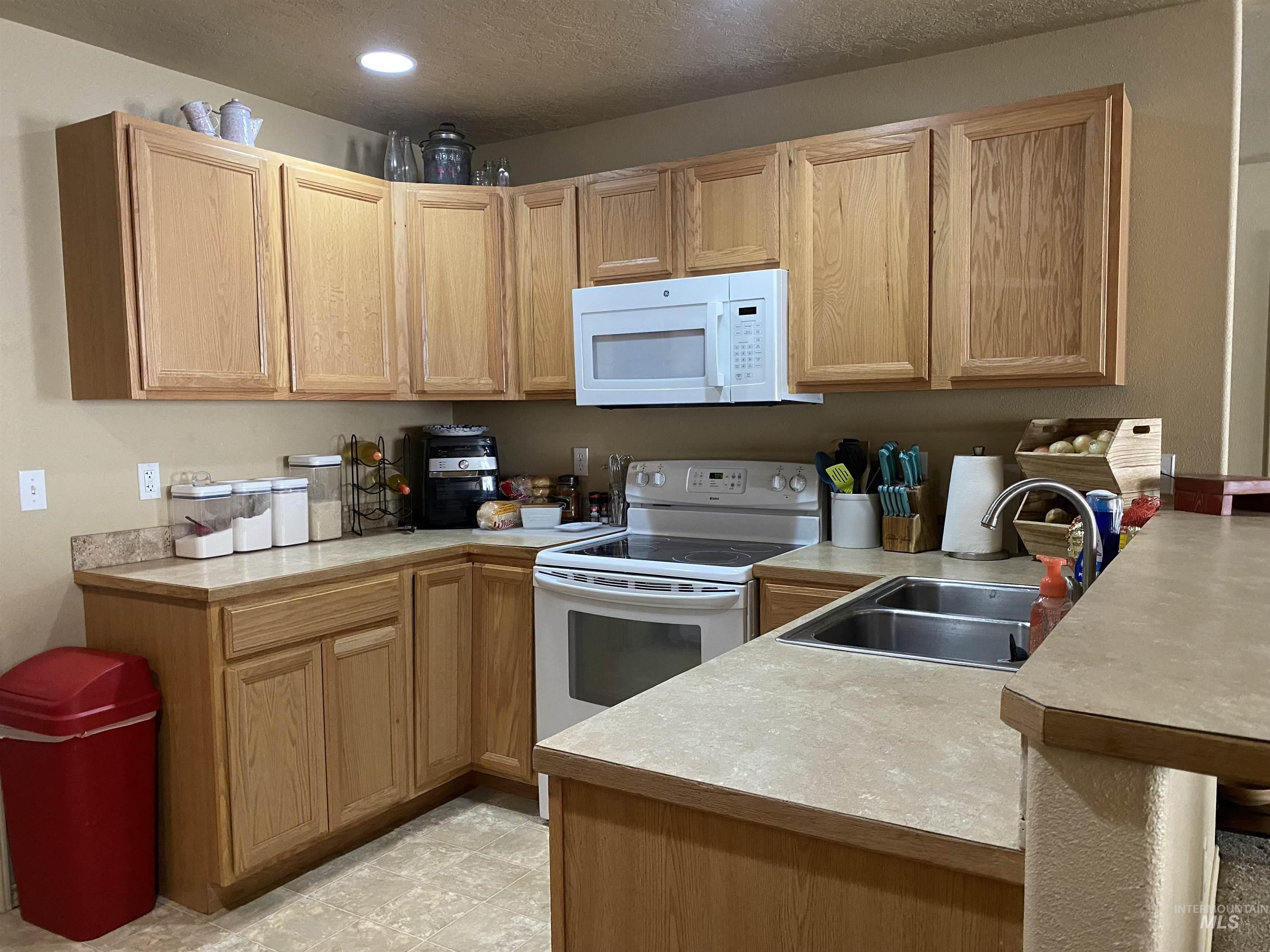Kitchen featuring light countertops, white appliances, a peninsula, a textured ceiling, and light brown cabinets